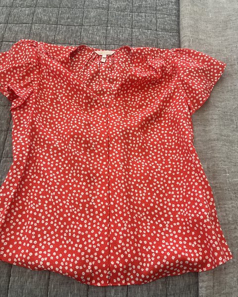 A red short-sleeved blouse with tiny cream flowers, laid flat on a gray quilt.