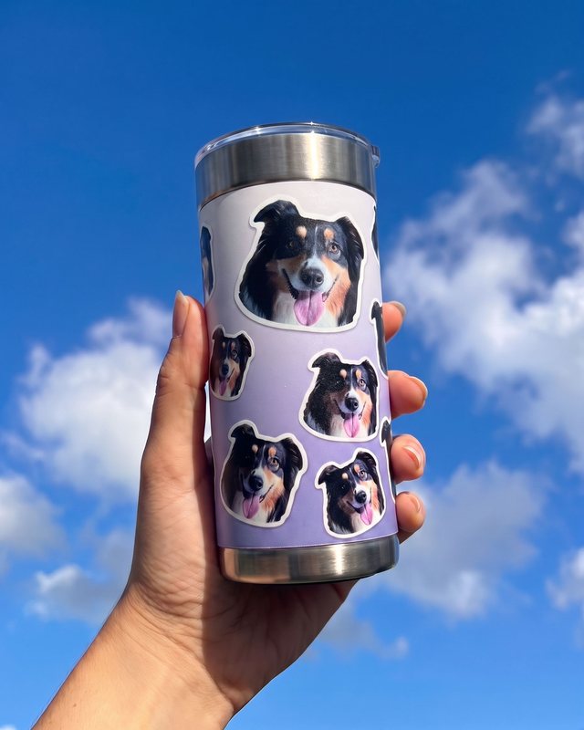 A hand holds Otto’s lavender sticker-face tumbler against a bright blue sky.